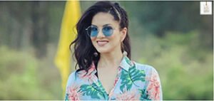 Sunny Leone smiling during a promotional event in a chic outfit, posing for the cameras.
