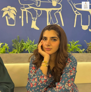 Vaneeza Sattar posing in a stylish pink outfit at a modern café, showcasing her elegant look and rising presence in the Pakistani entertainment industry.